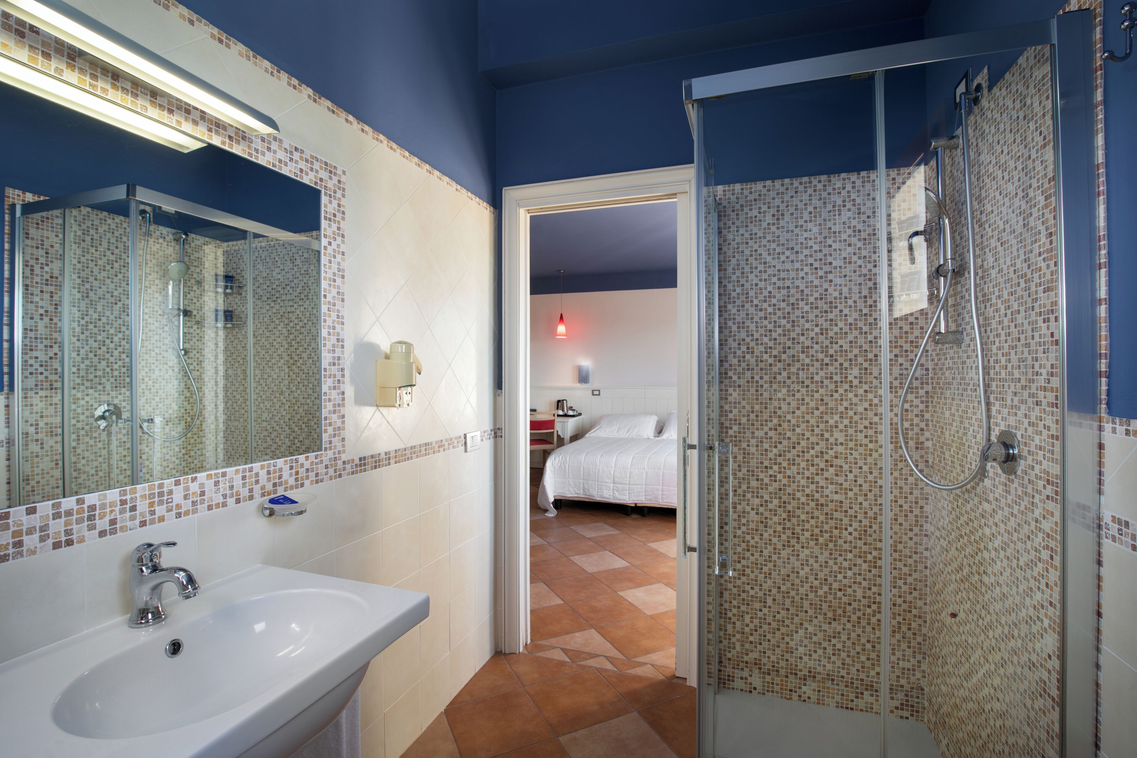 A bathroom with a sink, mirror, shower, and tiled walls.
