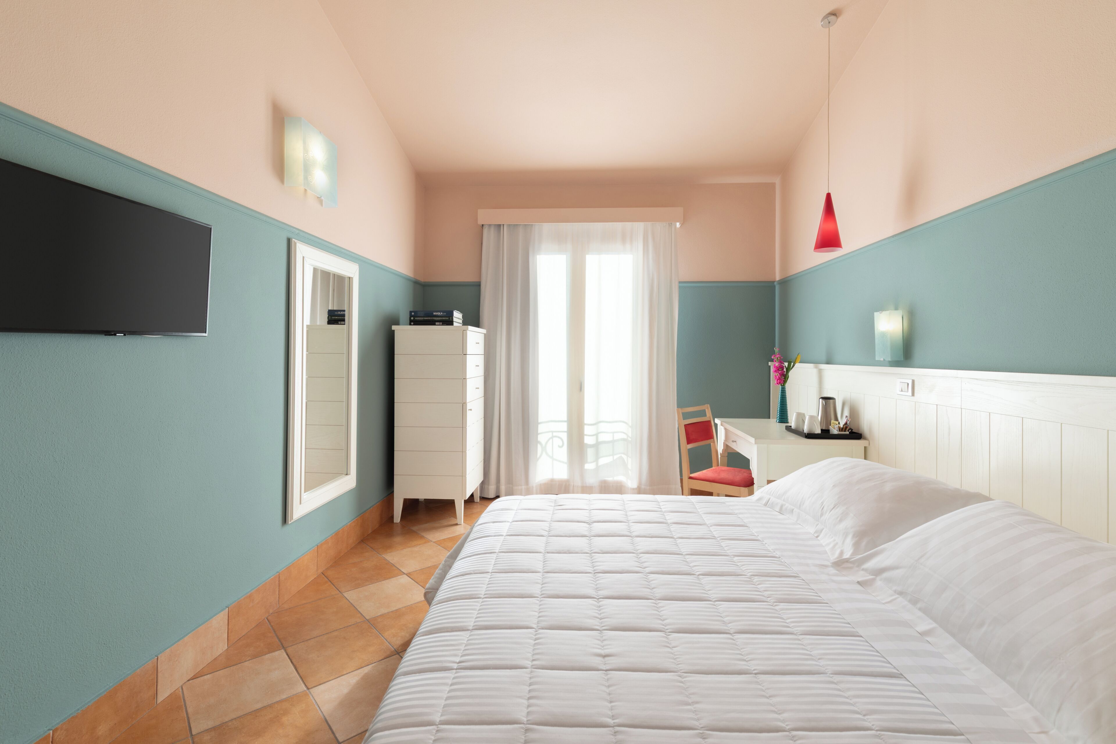 Une chambre à coucher avec un lit, une commode, un téléviseur et une fenêtre avec des rideaux.