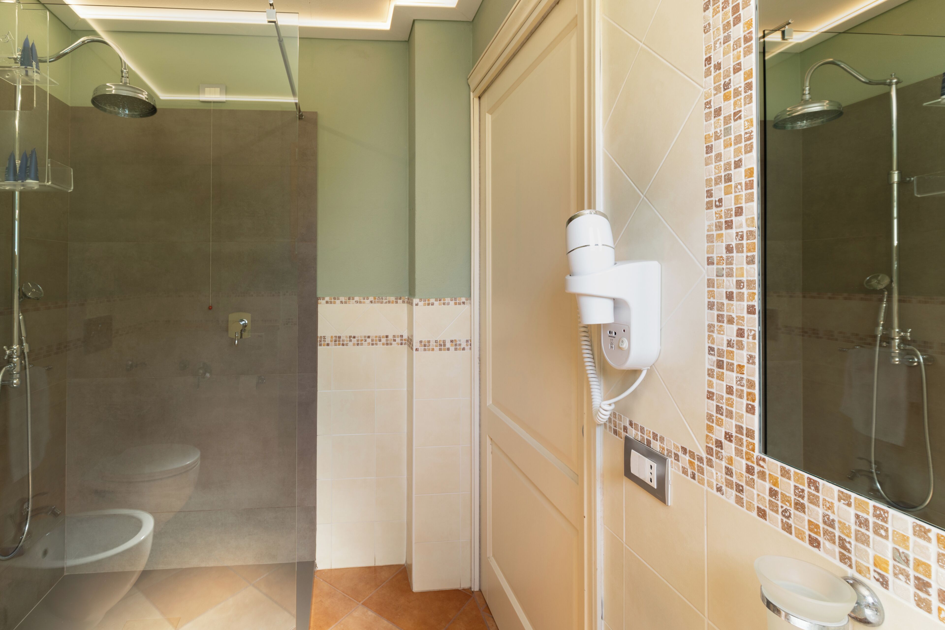 Un baño con ducha, inodoro y secador de pelo montado en la pared.