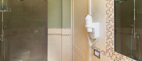 Un baño con ducha, inodoro y secador de pelo montado en la pared.