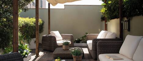 A covered outdoor seating area with wicker furniture, a tray with lemons, and a book.