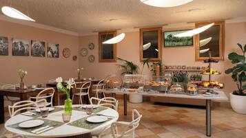 A dining area with round tables, chairs, and a buffet with various food items.