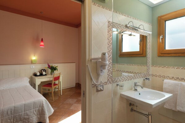Une chambre d’hôtel comprenant un lit, un bureau, une chaise et une salle de bain avec un lavabo, un miroir et une douche.