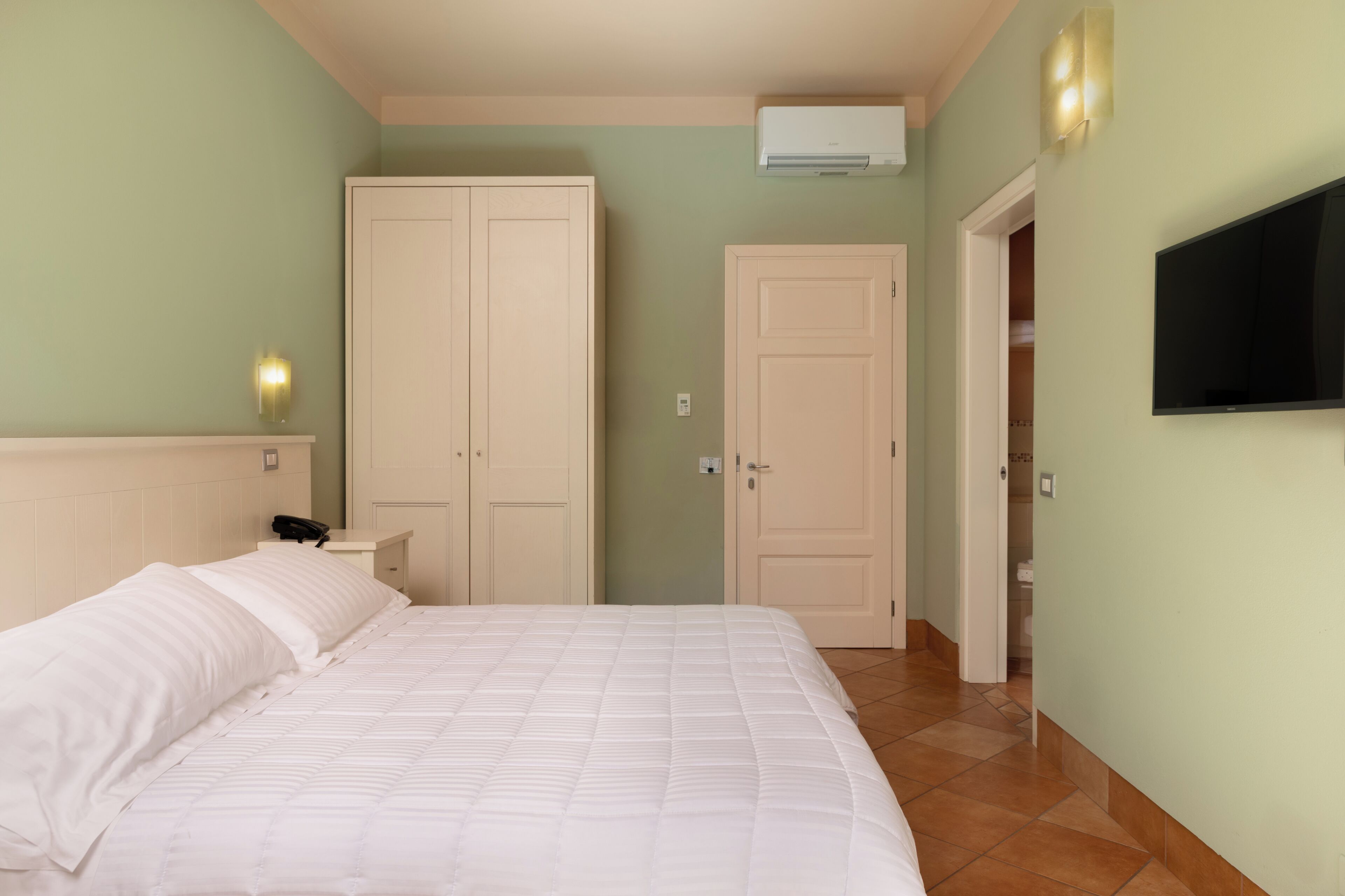 A bedroom with a bed, wardrobe, and a TV mounted on the wall.