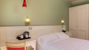 A hotel room with a bed, a desk with a chair, a red hanging light, and a wardrobe.