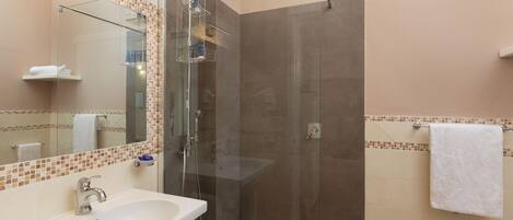 A bathroom with a glass-enclosed shower, a sink, a mirror, and a towel rack.