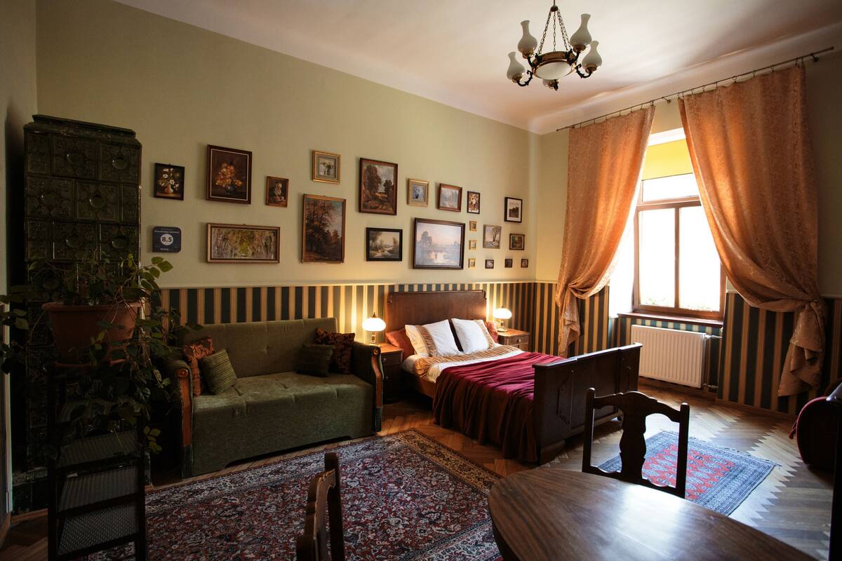 A cozy room with a bed, a sofa, a dining table, and a chandelier.