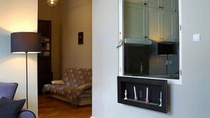 A living room with a herringbone wooden floor, a sofa, a lamp, and a large window with a kitchen visible through it. - Boutique Apartments - Kazimierz (Kraków)