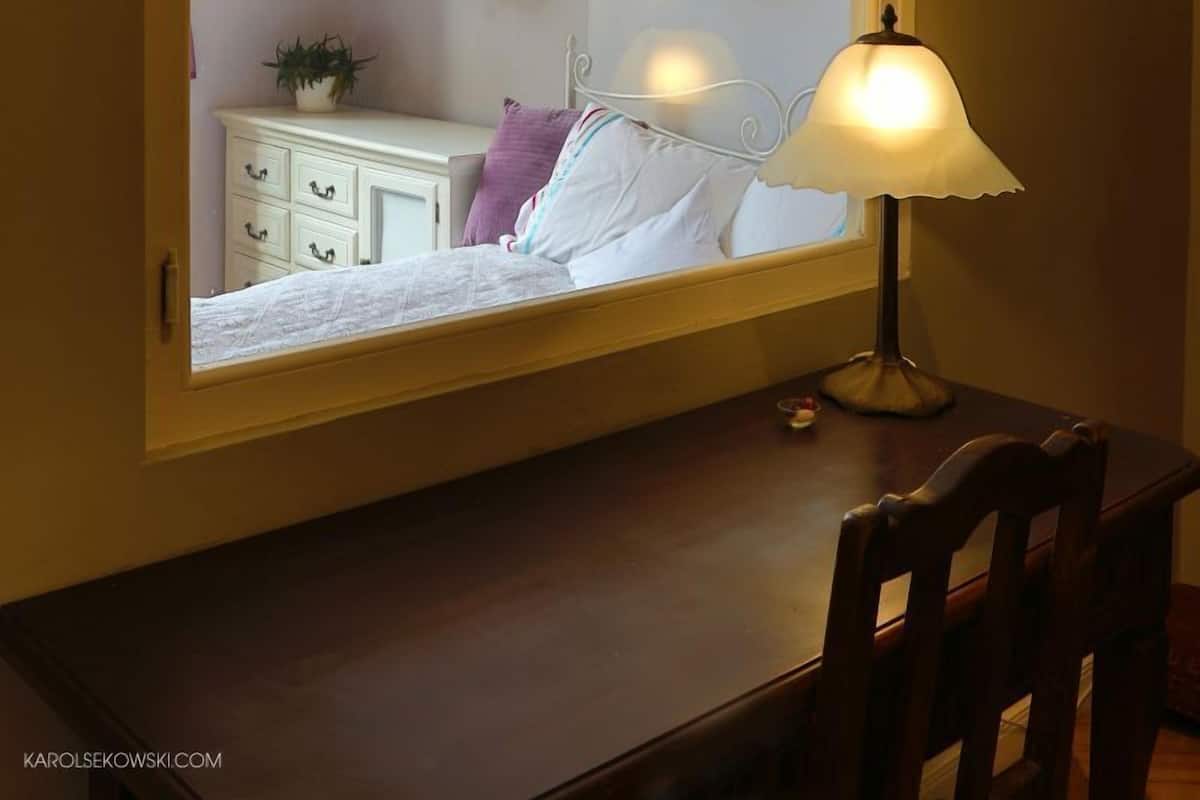 A bedroom with a bed, bedside table, lamp, and wall-mounted shelf with plants.