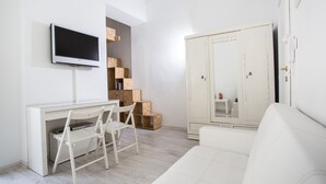 A modern, minimalist room with a white desk, a flat-screen TV, a white sofa, and a wardrobe. - Boutique Apartments - Kazimierz (Kraków)