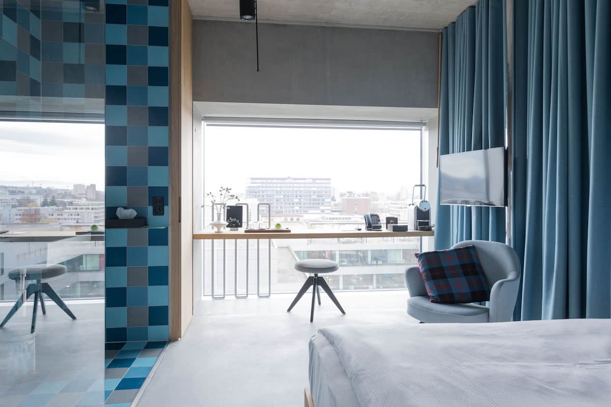 Une chambre d’hôtel moderne avec une grande fenêtre, un lit, un bureau et une chaise.