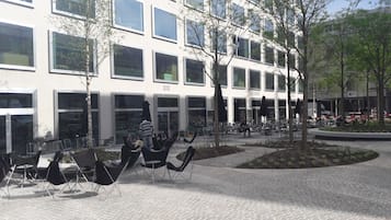 Een terras met stoelen en tafels, een gebouw met meerdere ramen en borden, en een aangelegde tuin.