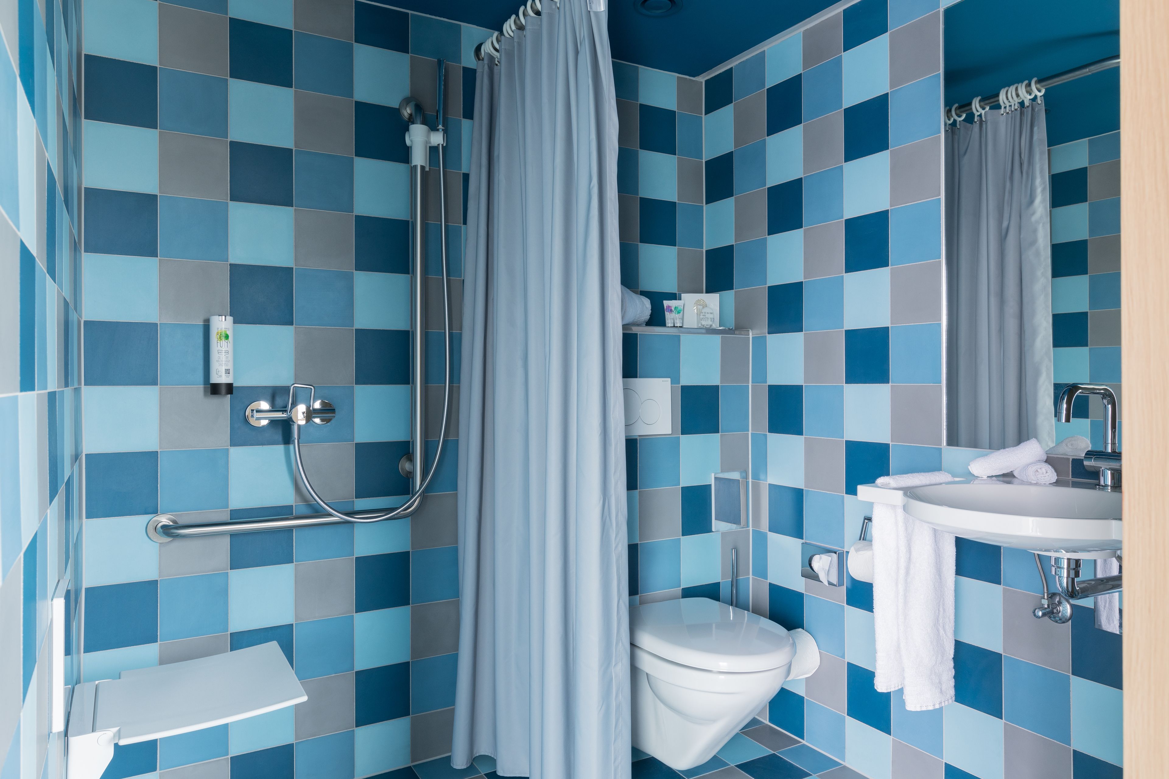A bathroom with a blue and gray checkered tile pattern, a white toilet, a sink with a mirror, and a shower with a curtain.