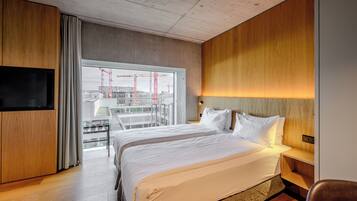 Een moderne hotelkamer met een groot bed, een televisie en een balkon met uitzicht op bouwkranen.