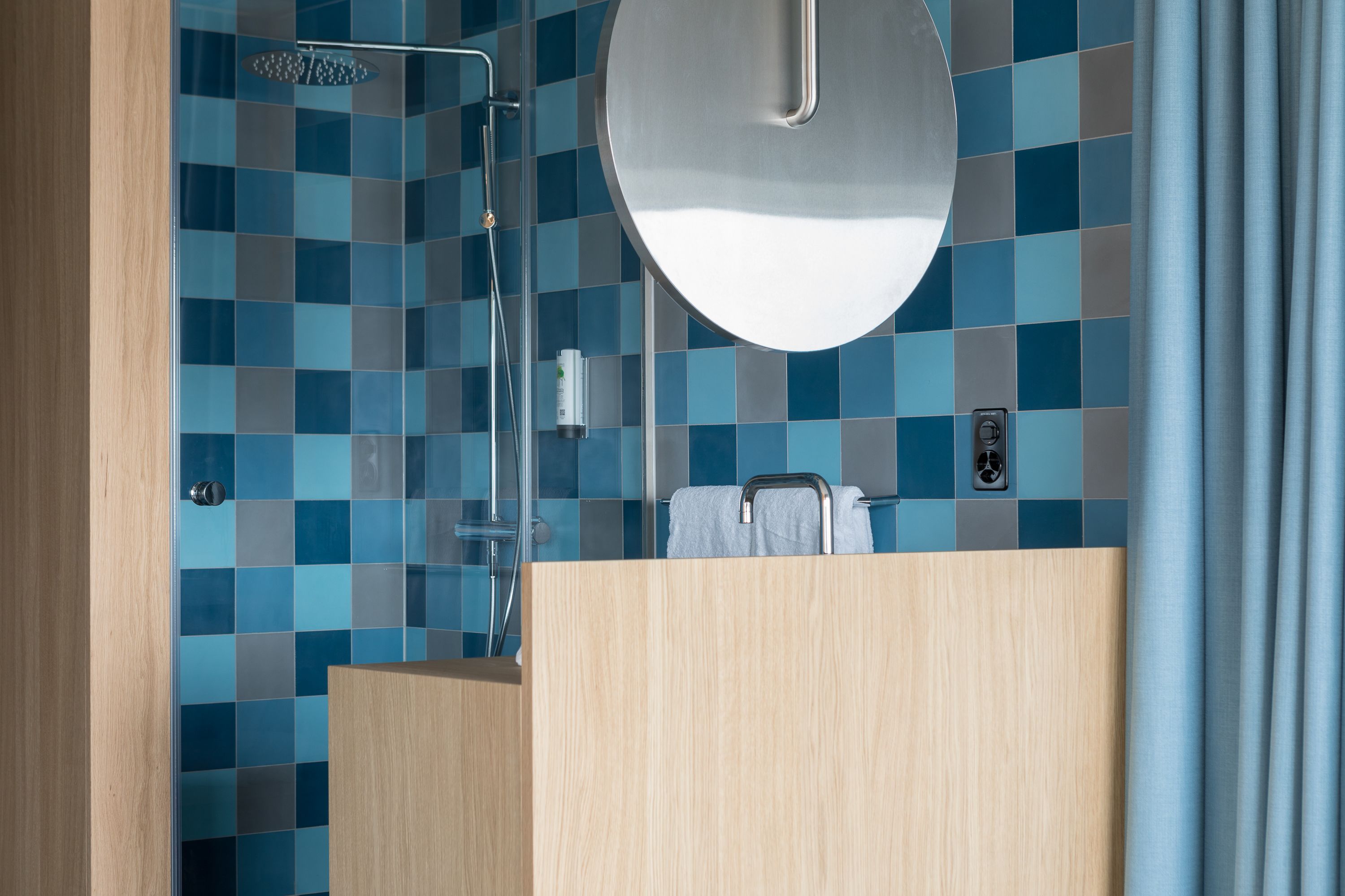 Une salle de bain moderne avec une douche, un miroir rond et un porte-serviettes.