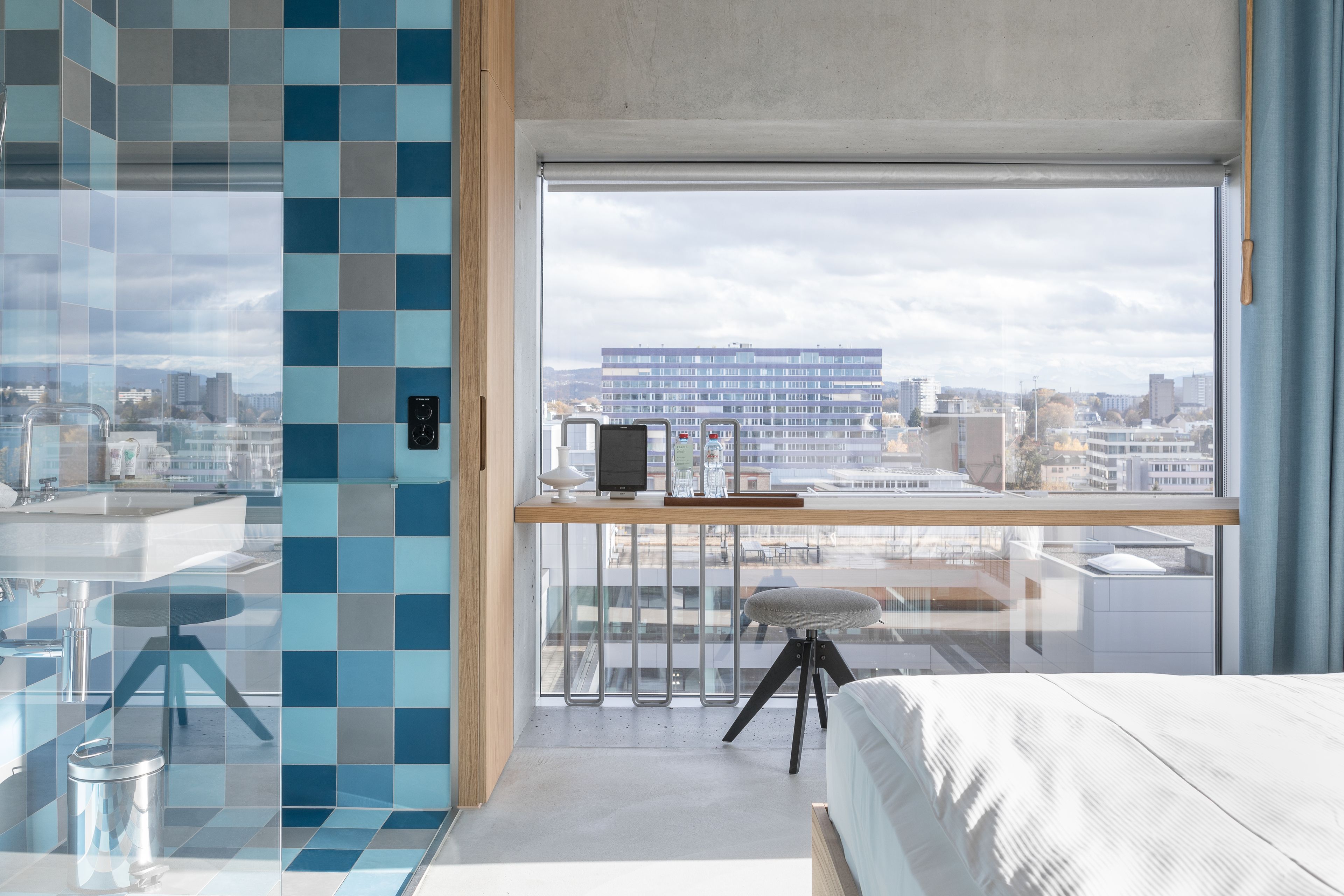 Un dormitorio moderno con un ventanal grande, un escritorio con computadora y vistas a la ciudad.