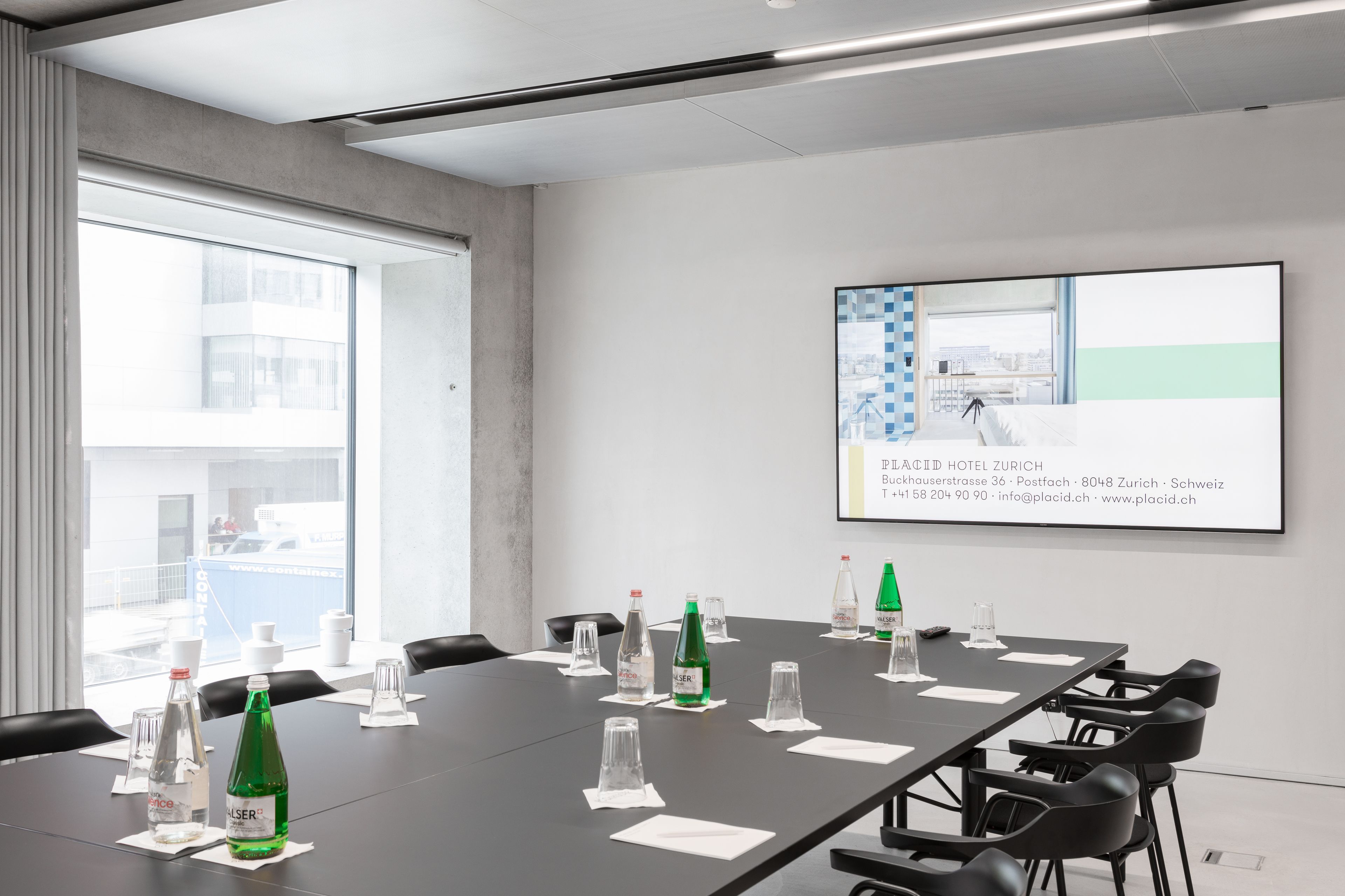 A conference room with a long table, chairs, water bottles, and a presentation screen.