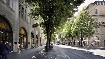 A tree-lined street with a tram, shops, and pedestrians.