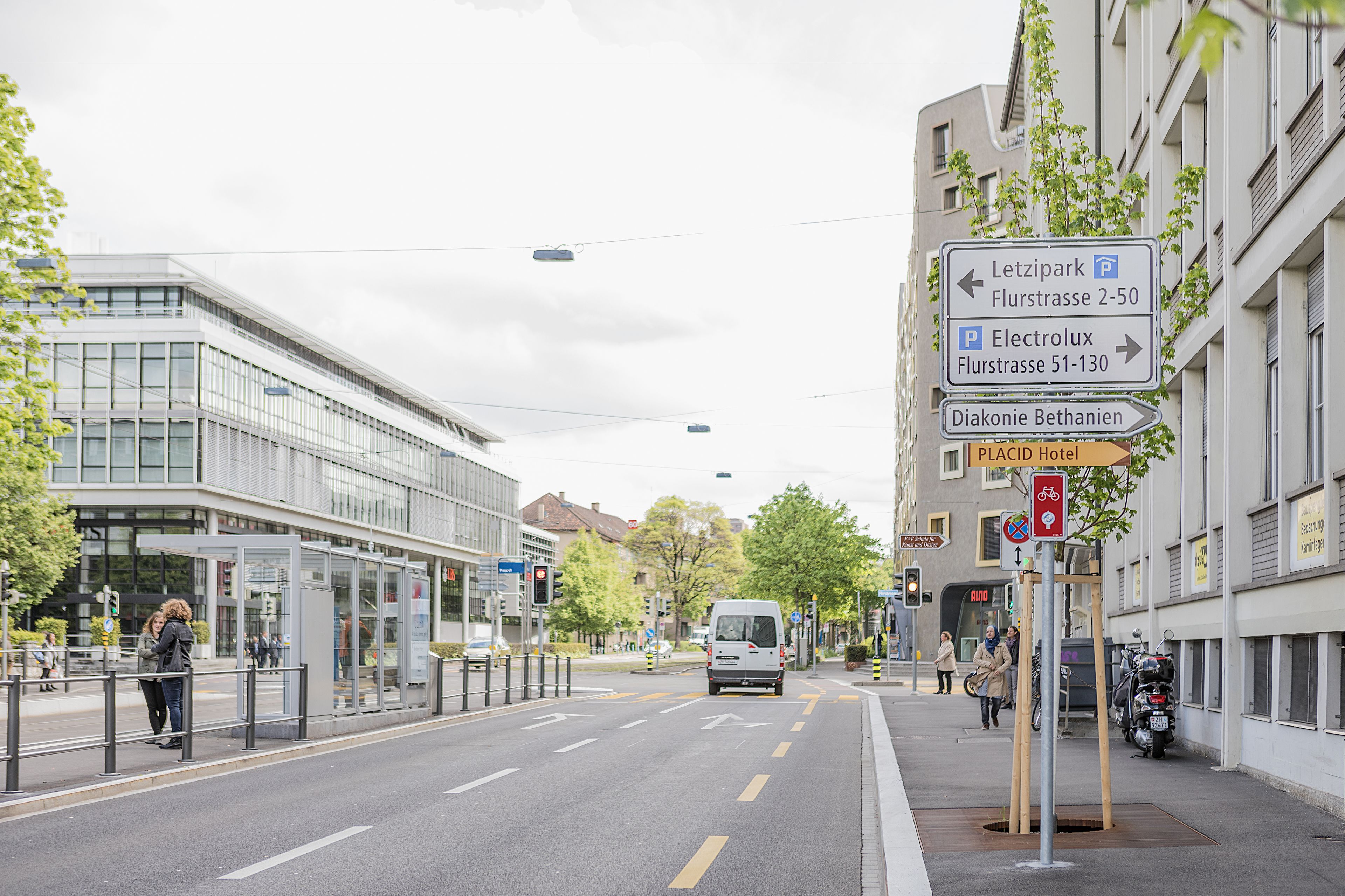 A street view with a bus stop, directional signs, and a building with a modern design.