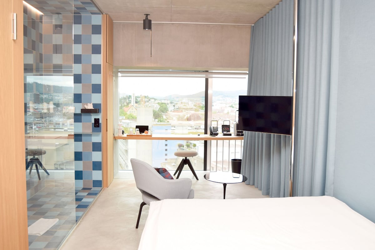 Une chambre d’hôtel moderne dotée d’un grand lit, d’un bureau avec un ordinateur, d’une télévision et offrant une vue sur la ville.