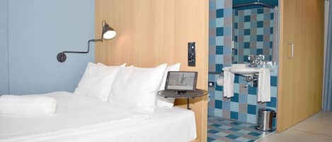 Ett hotellrum med en säng, ett nattduksbord, en lampa och utsikt in i badrummet.