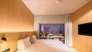 Une chambre d’hôtel moderne dotée d’un grand lit, d’un bureau avec une chaise, d’un téléviseur à écran plat et offrant une vue sur la ville la nuit.