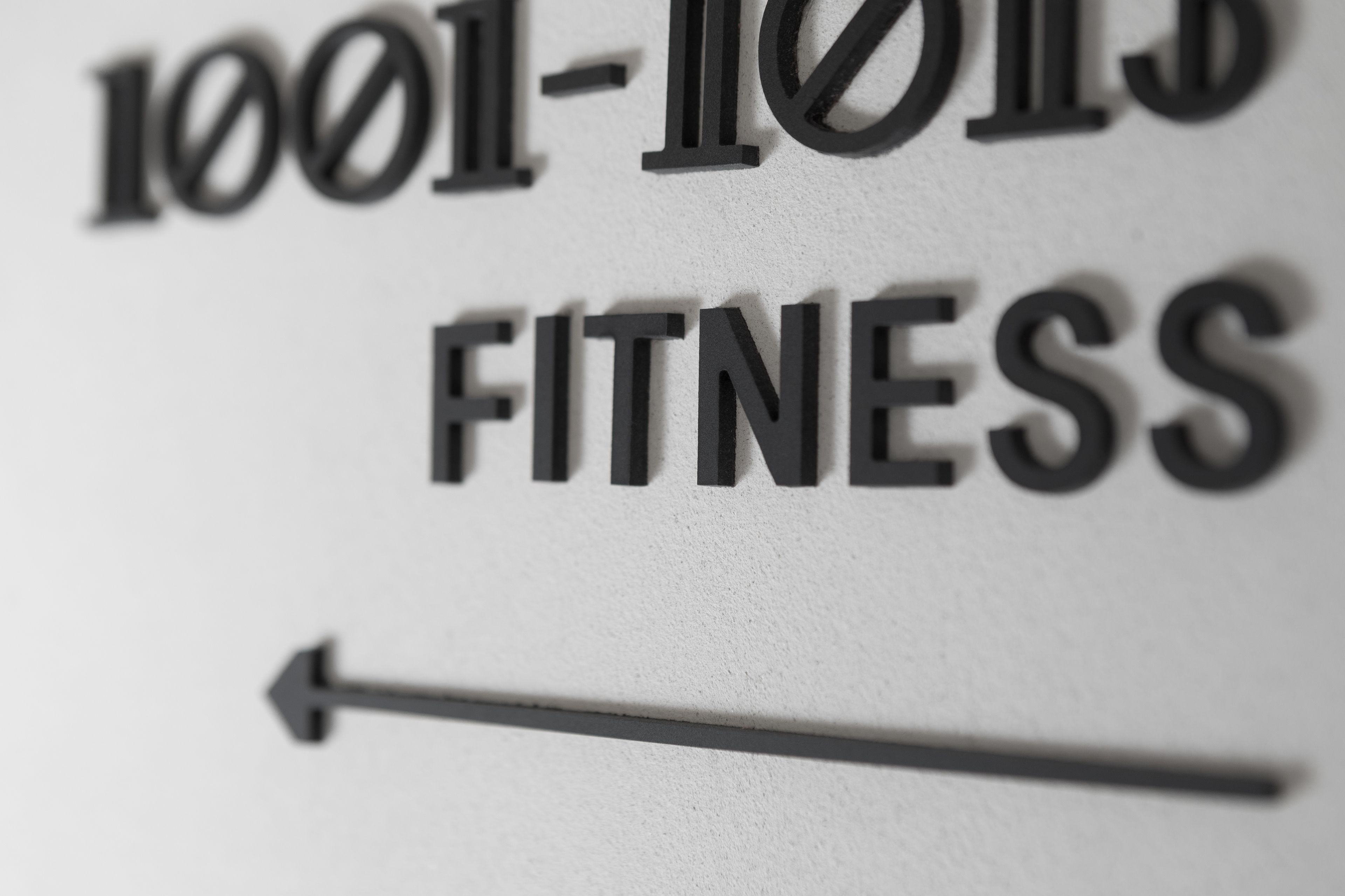 Ein Schild mit dem Schriftzug '1001-1013 FITNESS' und einem nach links zeigenden Pfeil.