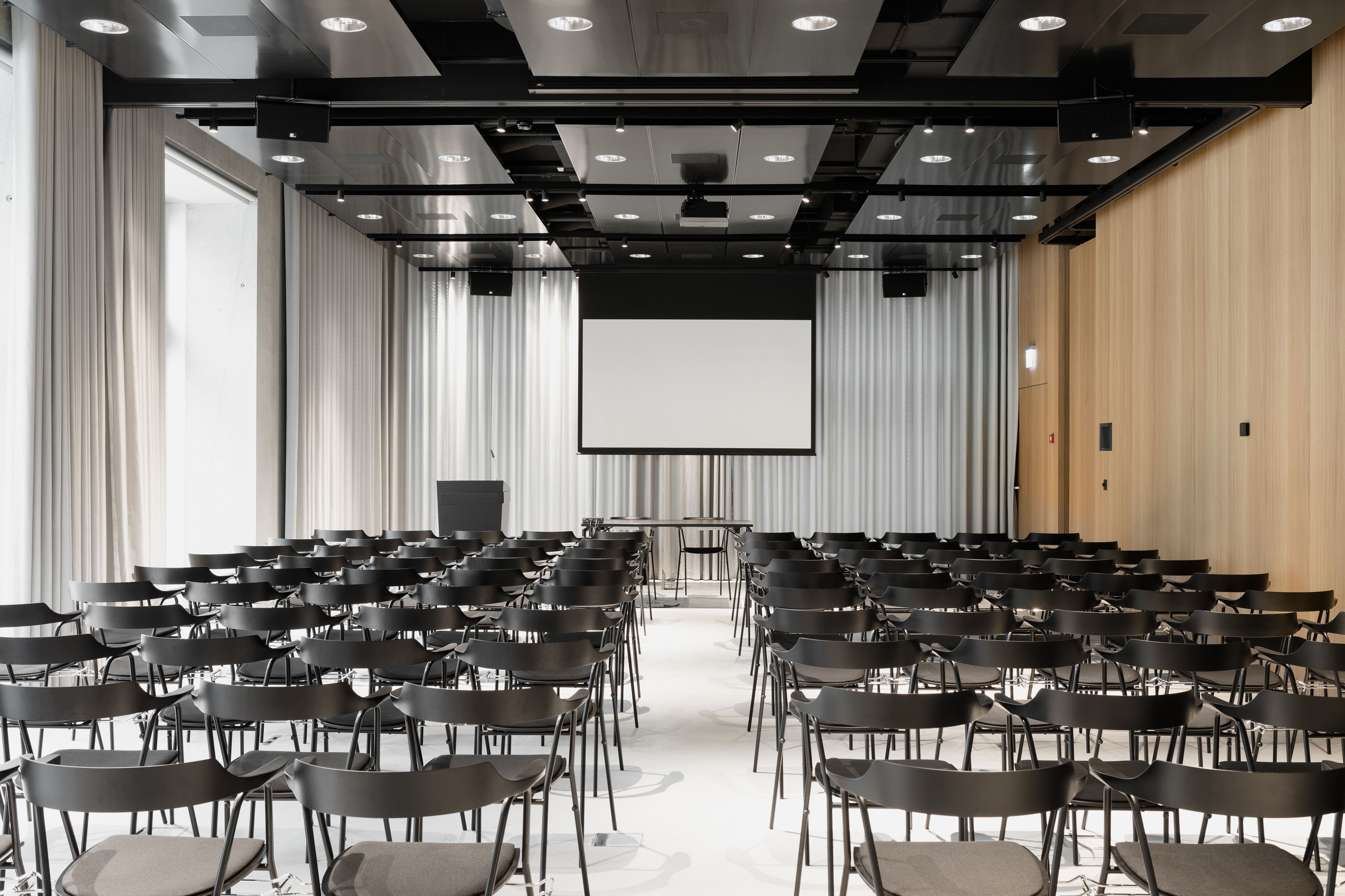 Un salón de conferencias con filas de sillas, una pantalla grande y un revestimiento de pared de madera.