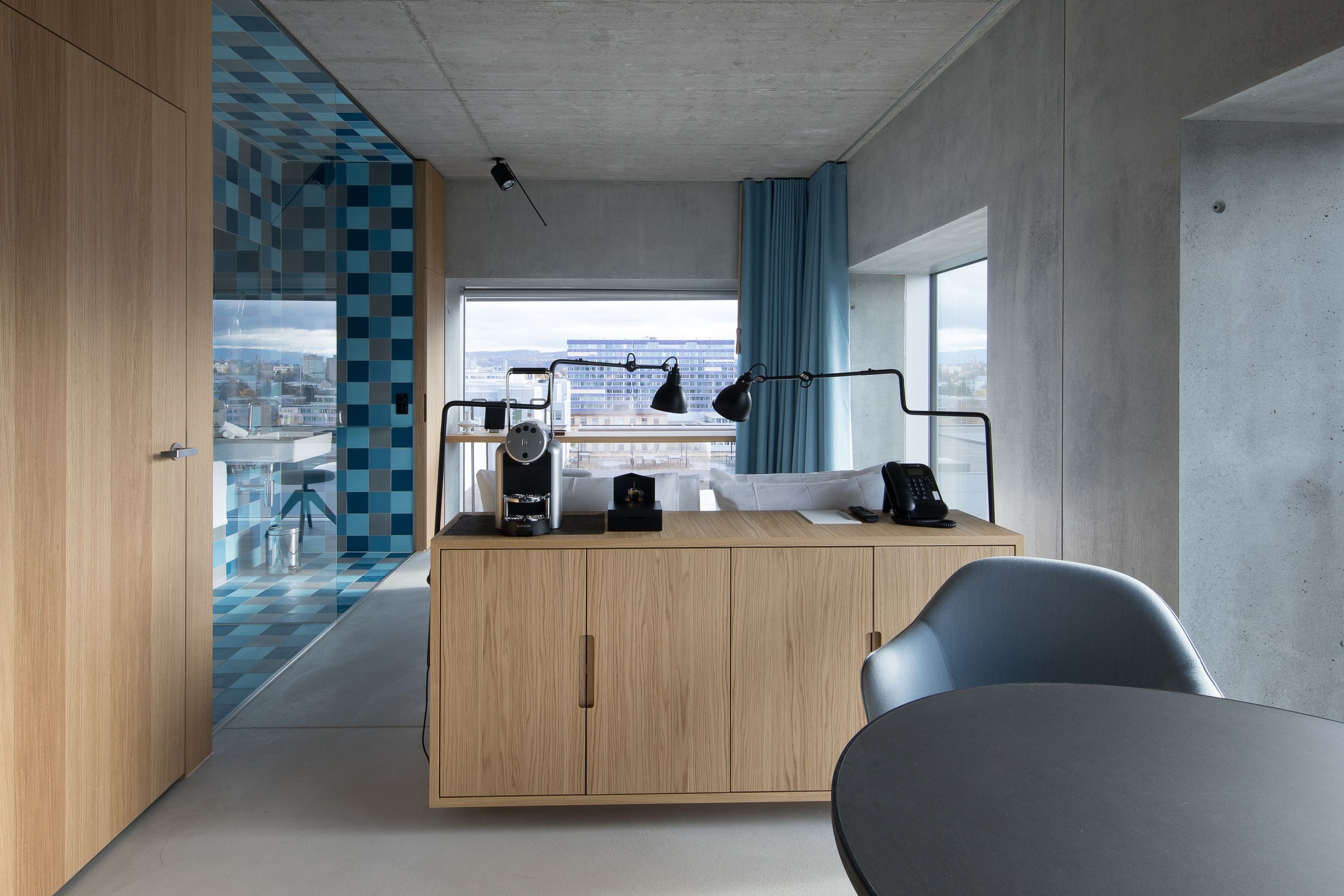 A modern kitchen with a wooden cabinet, a black countertop, and a view of the city through large windows.