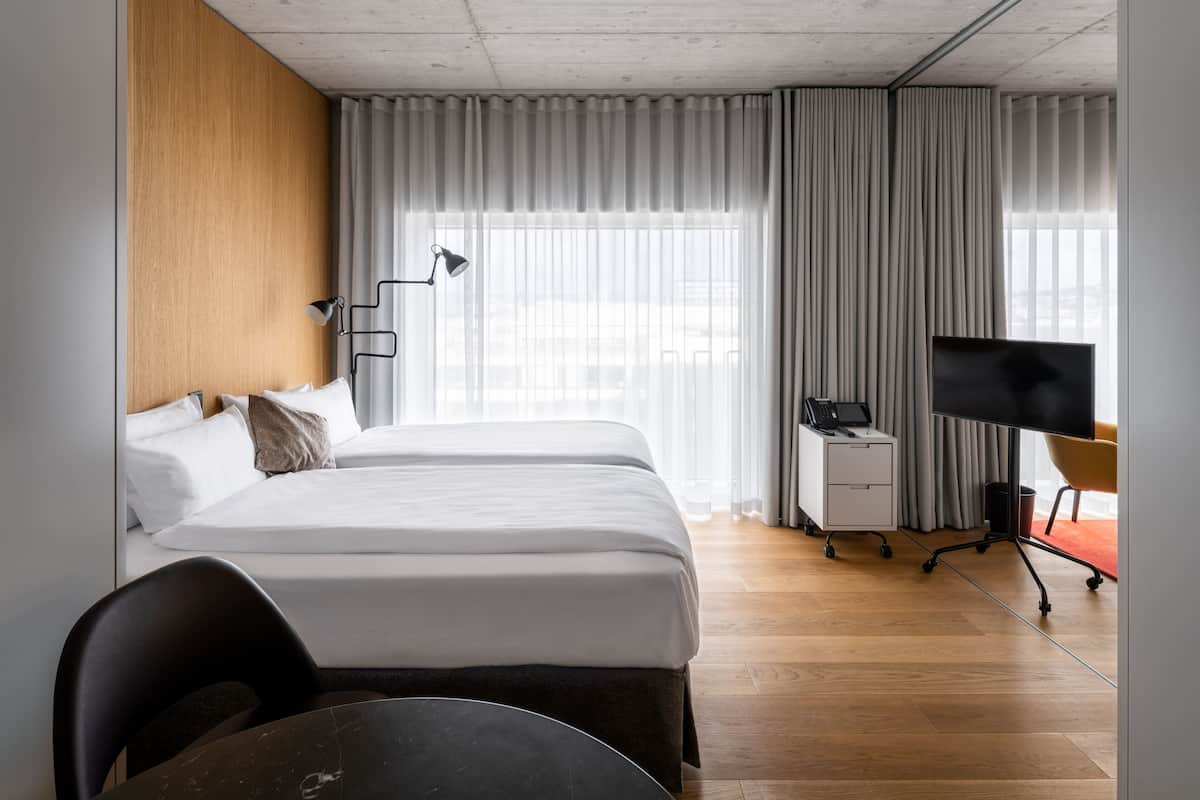 Une chambre d’hôtel avec deux lits, un bureau avec un ordinateur, une télévision et une chaise.