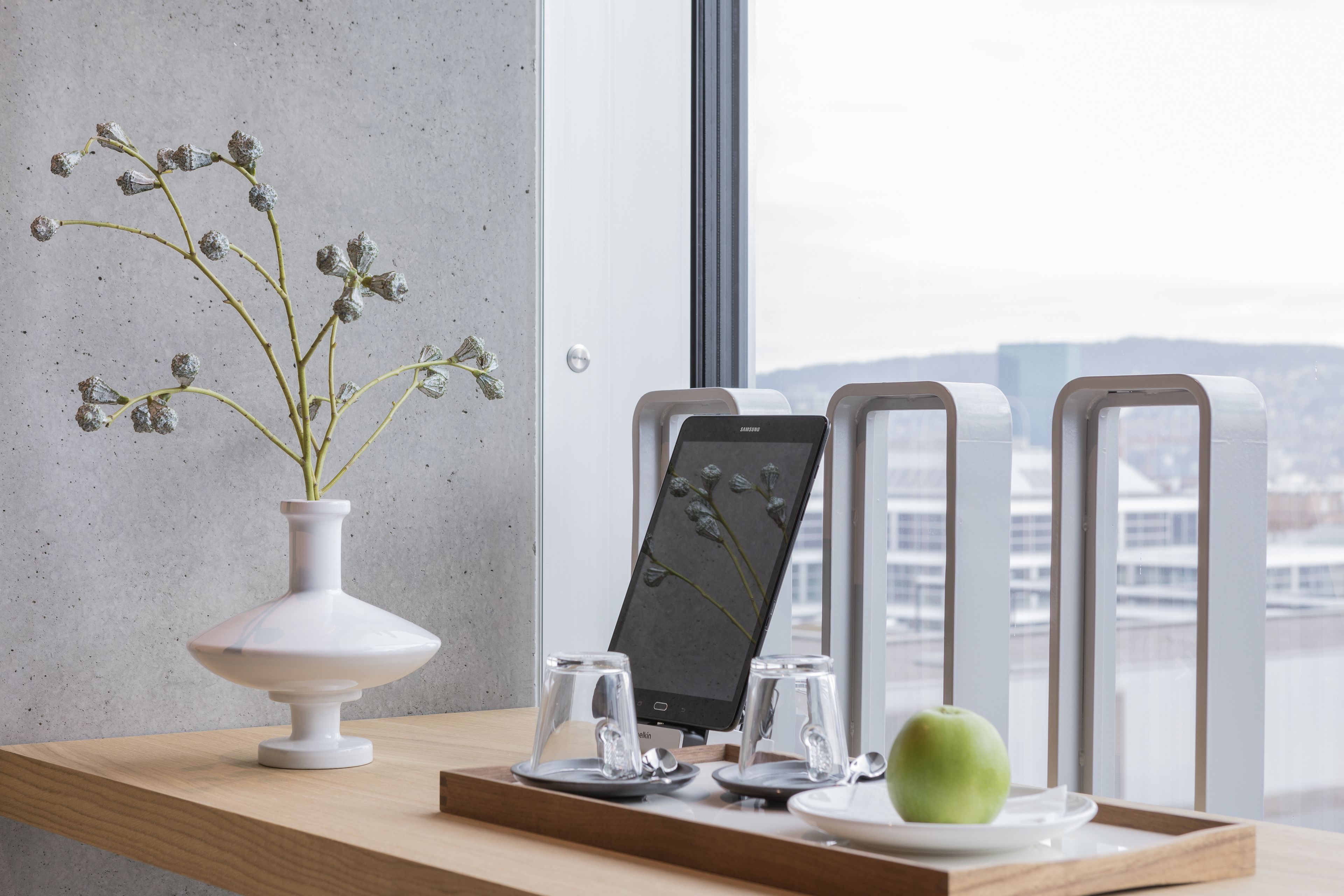 A modern interior with a white vase, a tablet, two glasses, and a green apple on a wooden table.