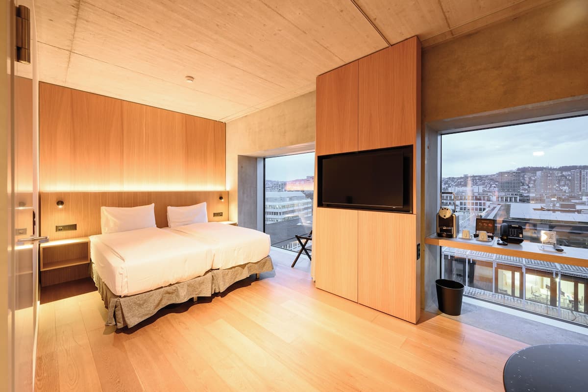Une chambre d’hôtel moderne avec un grand lit, des panneaux de bois, une télévision et une vue sur la ville.