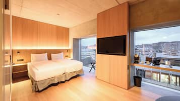 A modern hotel room with a large bed, wooden paneling, a TV, and a city view.