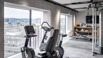 Ein modernes Fitnessstudio mit Cardiogeräten, einer Hantelbank und Blick auf die Stadt.