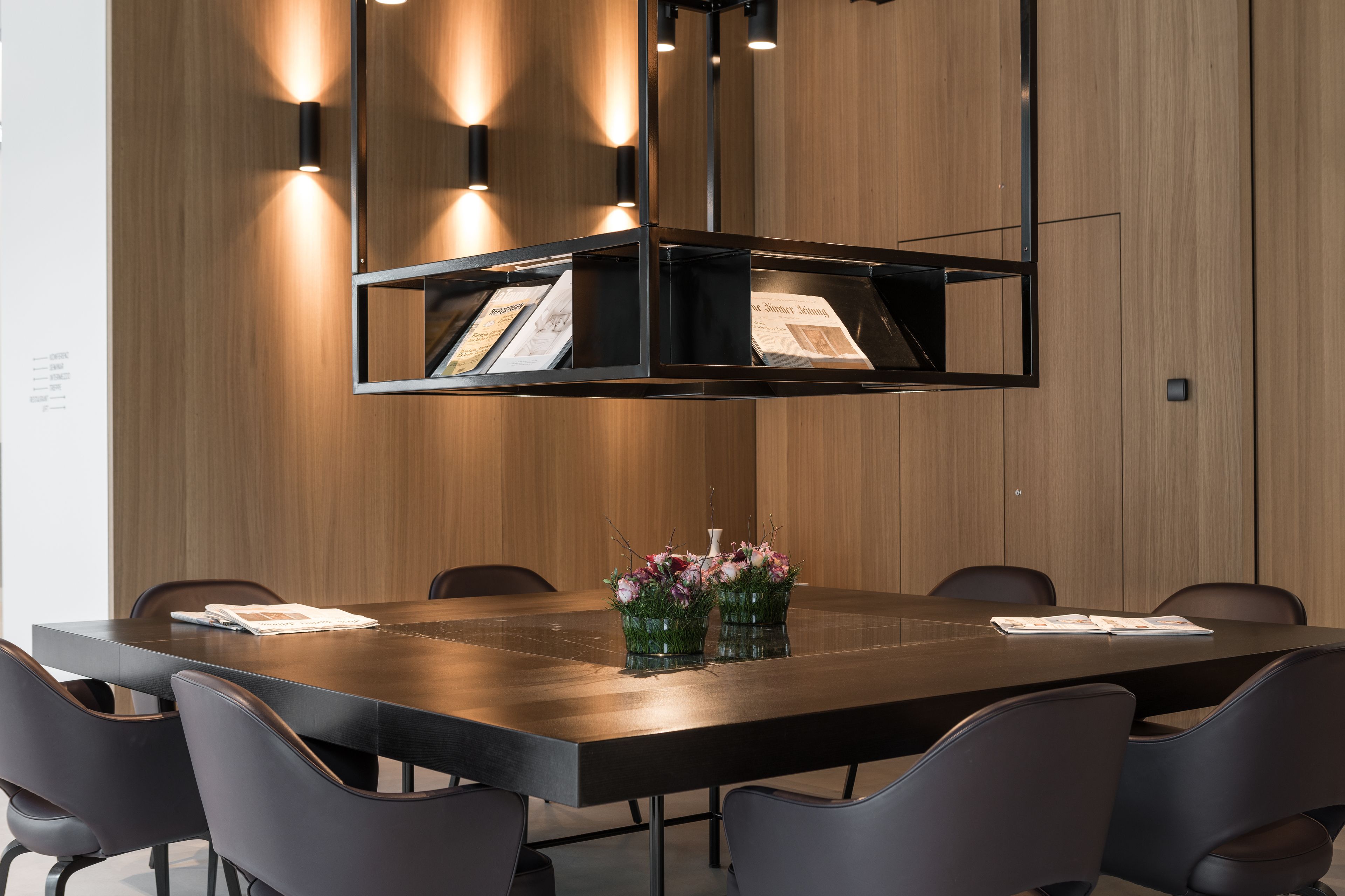 A conference room with a long table, black chairs, and a central light fixture.