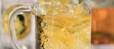 A clear glass mug with a handle, filled with a yellowish beverage, ice cubes, and garnished with a lemon slice and mint leaves.