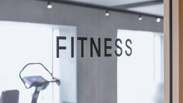 Ein Fitnessstudio-Innenraum mit einem stationären Fahrrad und einem Laufband, wobei das Wort 'FITNESS' gut sichtbar angebracht ist.