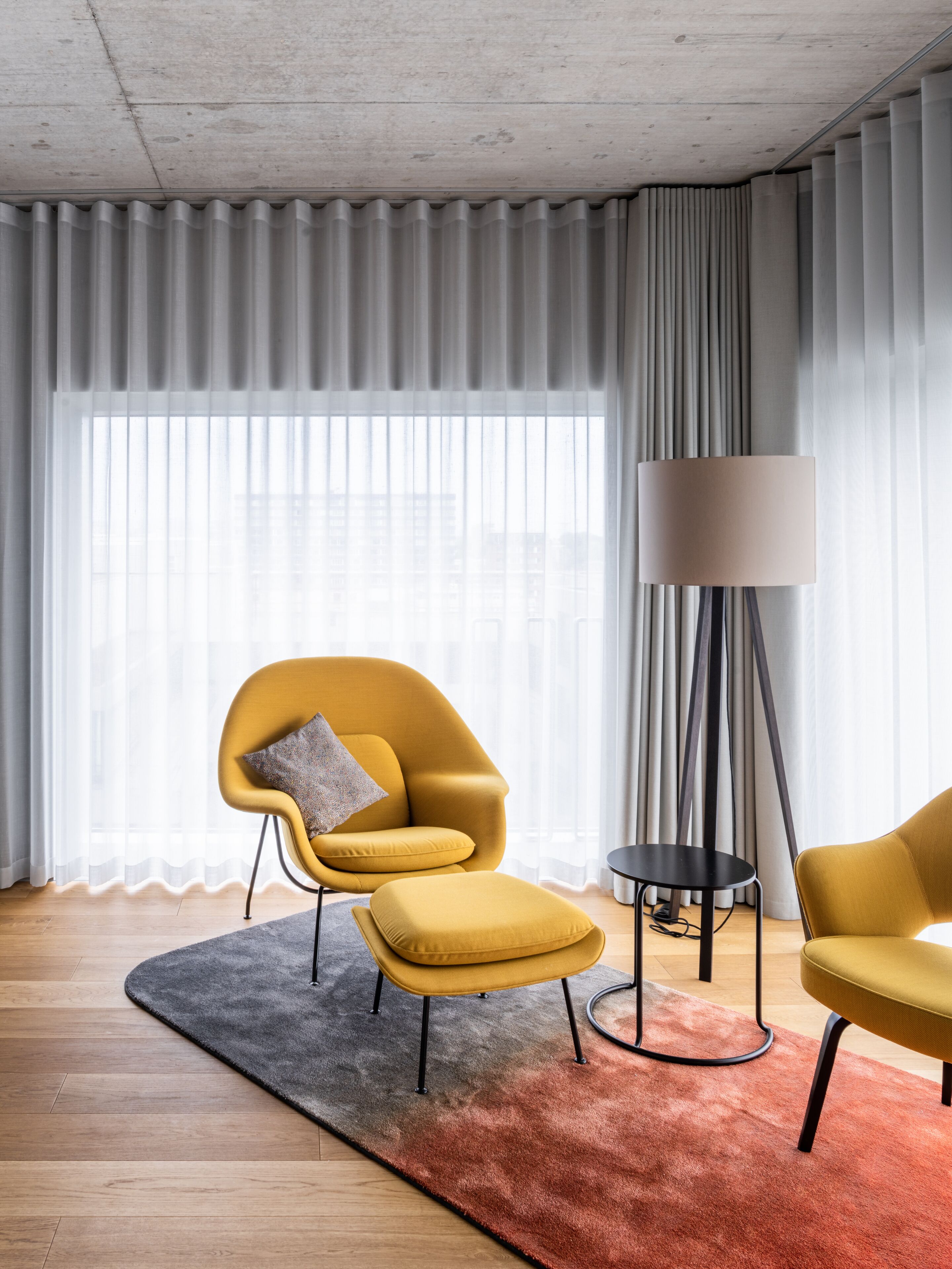 Un salon moderne avec un fauteuil jaune, un pouf et une lampe sur pied.
