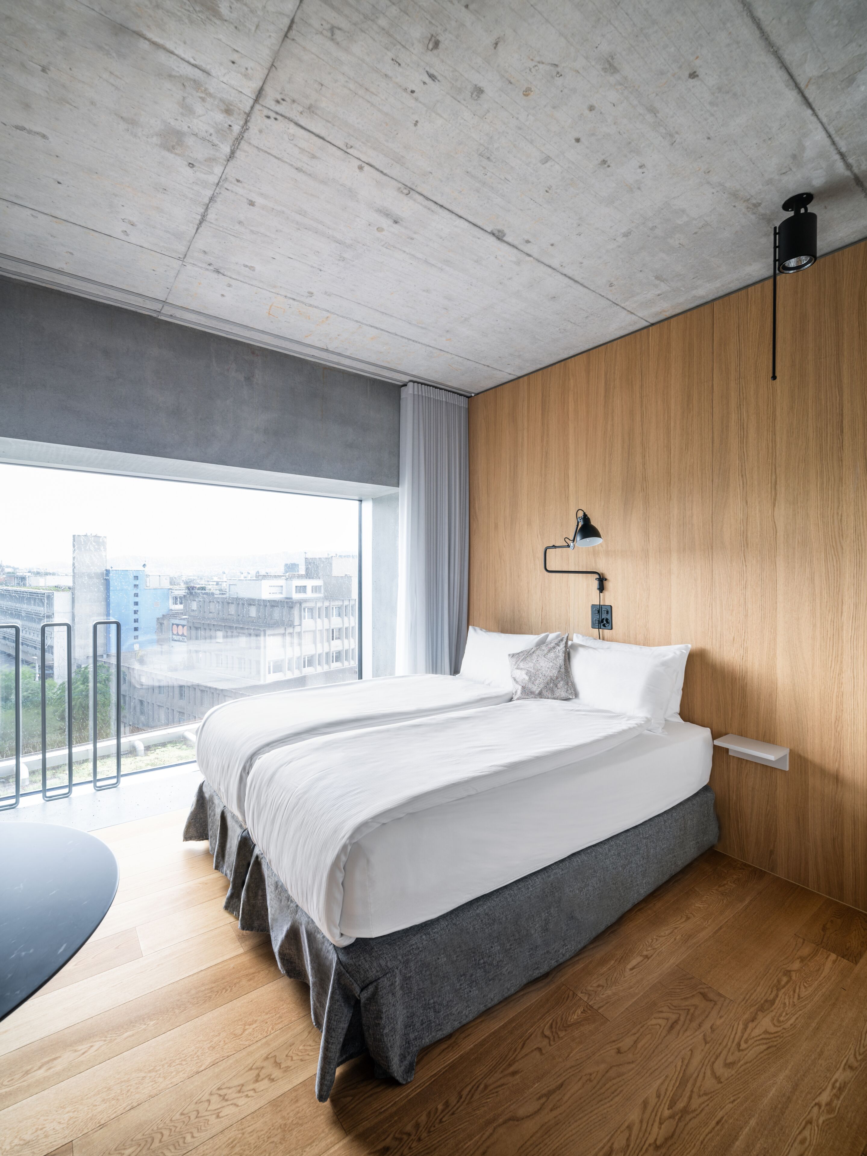 Une chambre moderne avec un grand lit, des murs recouverts de panneaux en bois, une vue sur la ville et un petit bureau.