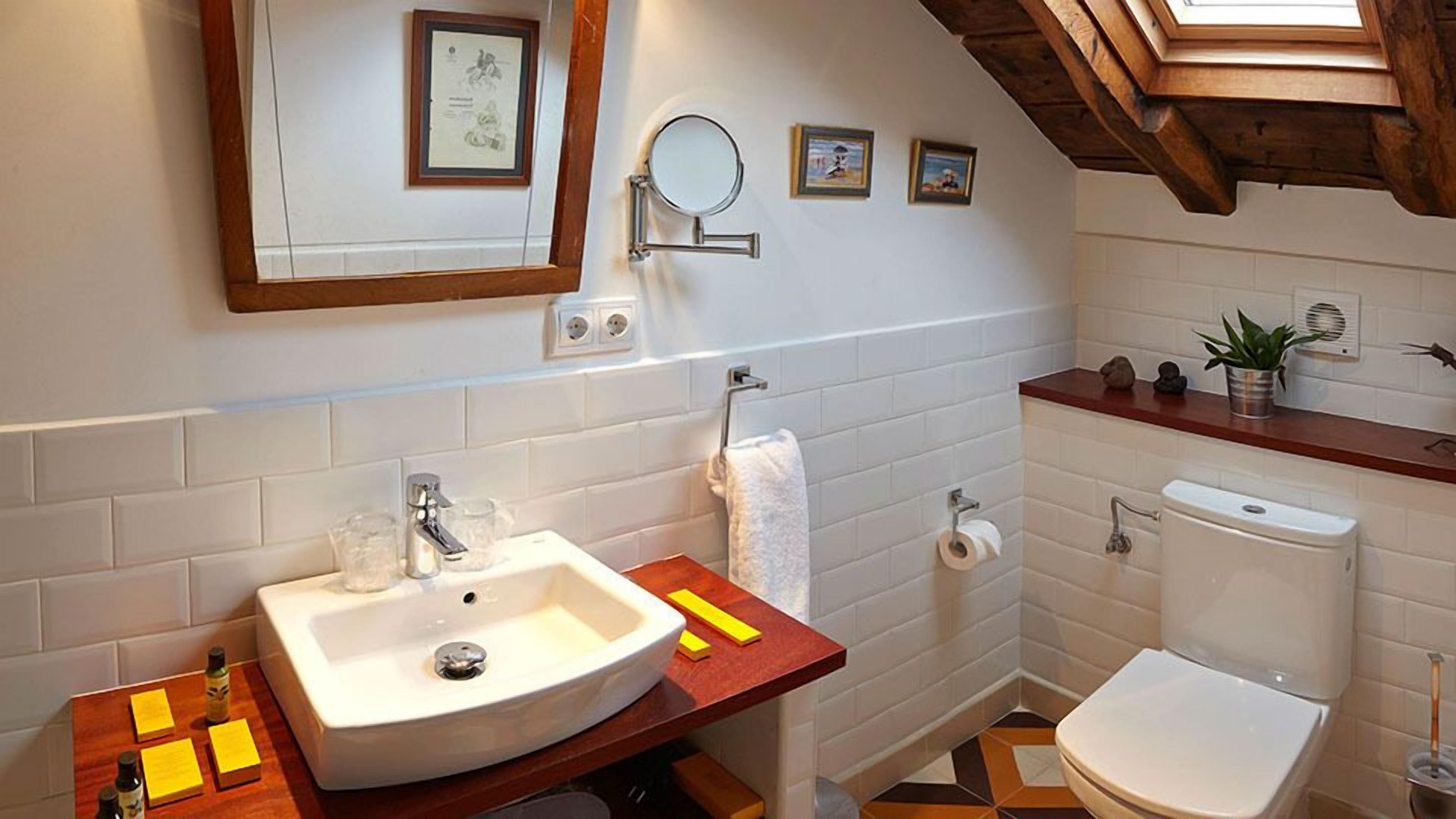 A bathroom with a white sink, mirror, and toilet. There are framed pictures on the wall, a towel hanging on a rack, and a small plant on the countertop.