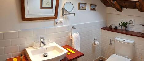 A bathroom with a white sink, mirror, and toilet. There are framed pictures on the wall, a towel hanging on a rack, and a small plant on the countertop.