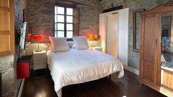 A bedroom with a stone wall, a wooden wardrobe, a bed with white linens, and two bedside lamps.