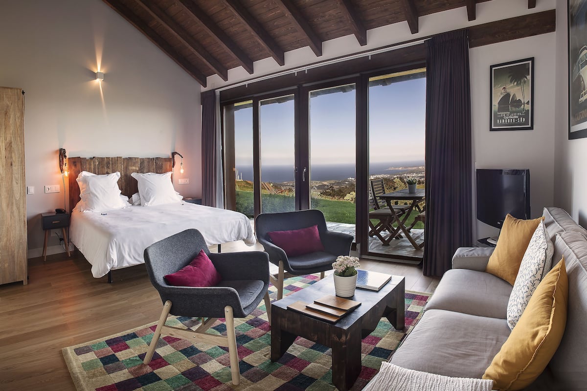 A bedroom with a large bed, a sitting area with a sofa and chairs, and a balcony with a view.