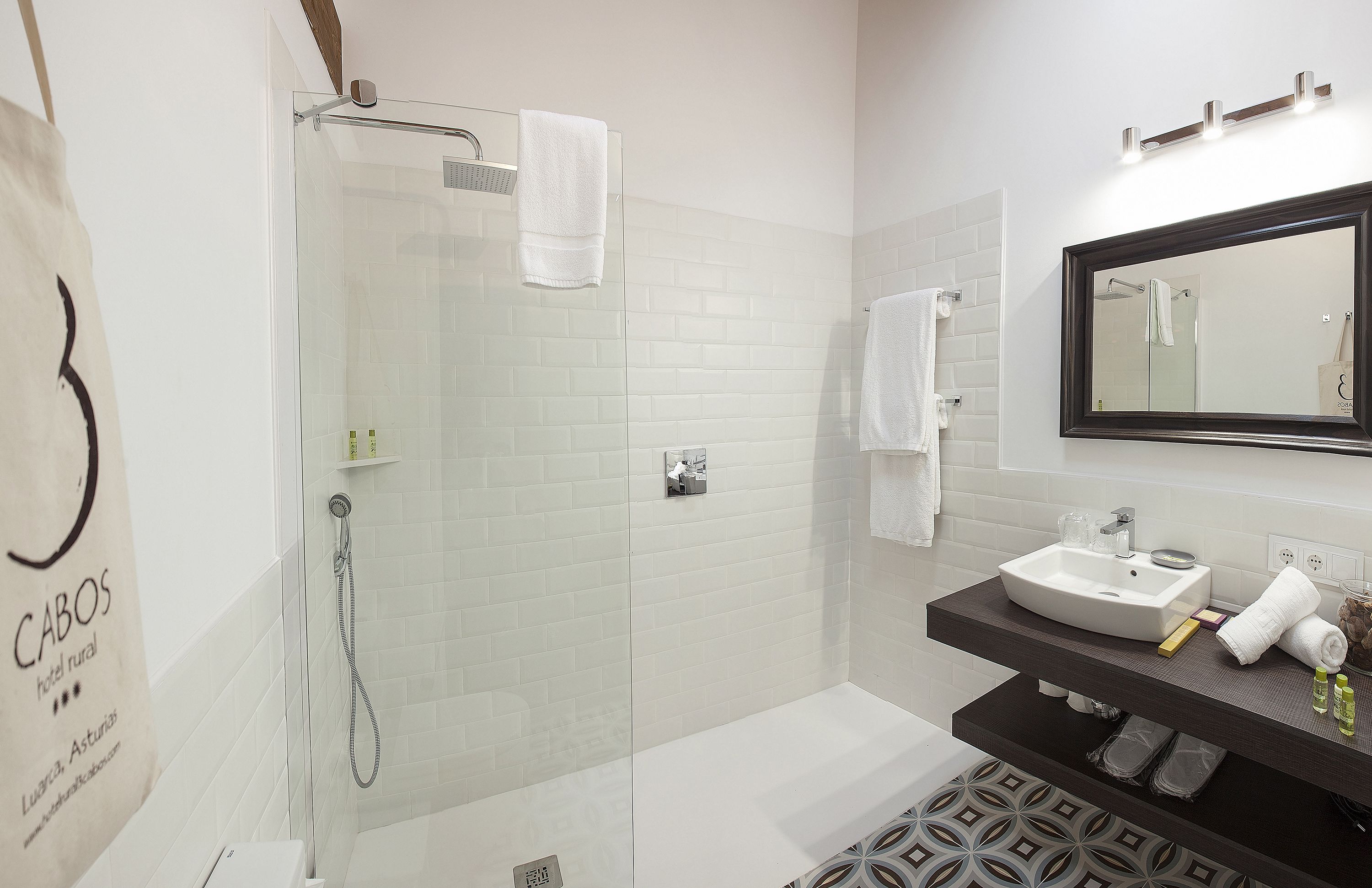 Un baño moderno con ducha de vidrio, tocador oscuro con espejo y paredes de azulejos blancos.
