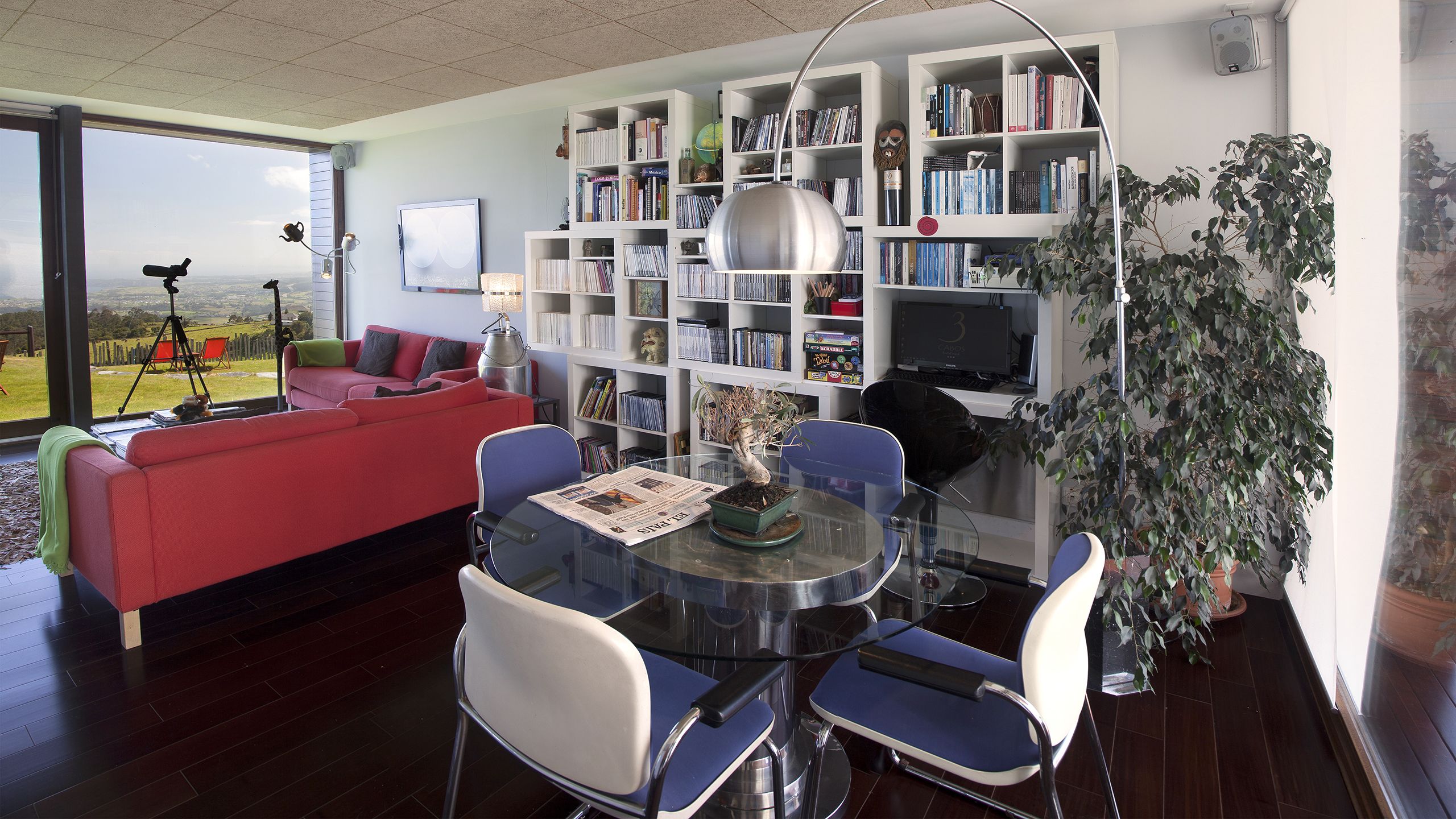 A modern living room with a red sofa, a glass coffee table, and a bookshelf filled with books.