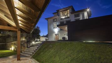 Una casa moderna con terraza de madera, escalones de piedra y exterior bien iluminado al anochecer.