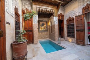 A courtyard with a swimming pool, wooden doors, and intricate wall patterns.