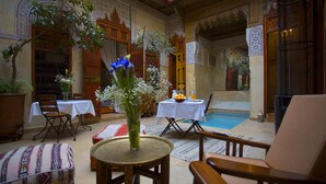 Un intérieur de style traditionnel agrémenté d’une piscine, de tables, de chaises et de plantes décoratives.