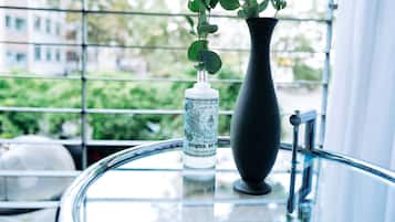 Una botella de agua de rosas en un florero negro sobre una mesa de vidrio junto a una ventana con vistas a edificios y follaje.