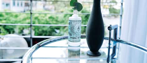 A bottle of rose water in a black vase on a glass table by a window with a view of buildings and greenery.